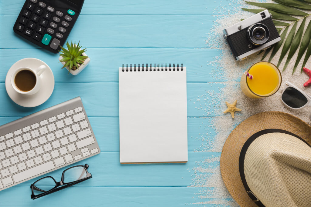 image de bureau, ordi, boissons, lunettes, chapeau qui fait penser au voyage